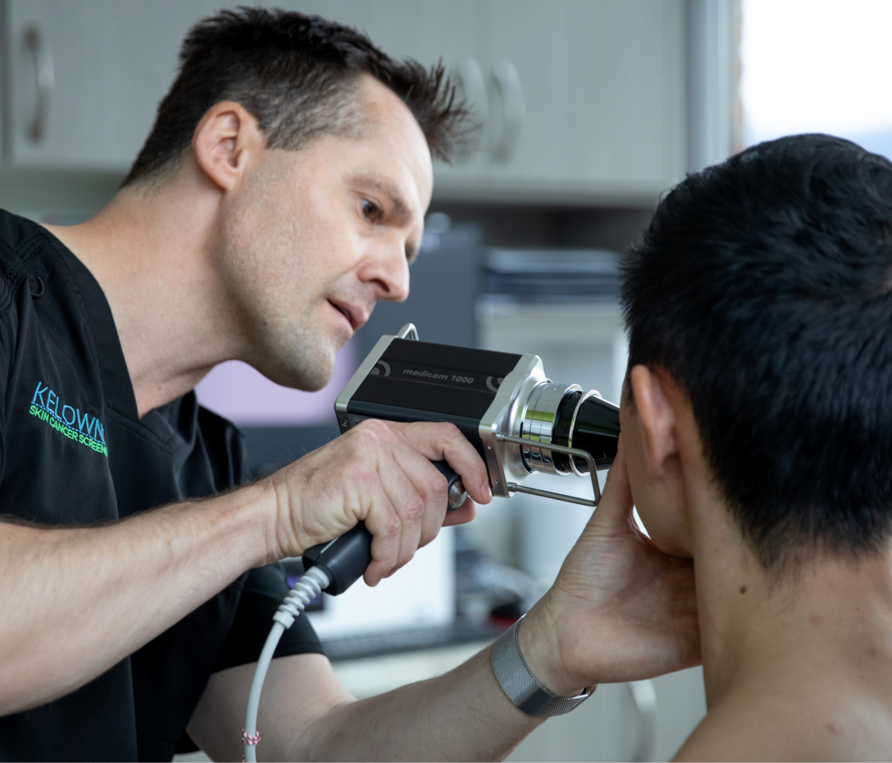 A clinician examines a patient's face with a handheld dermatoscope.
