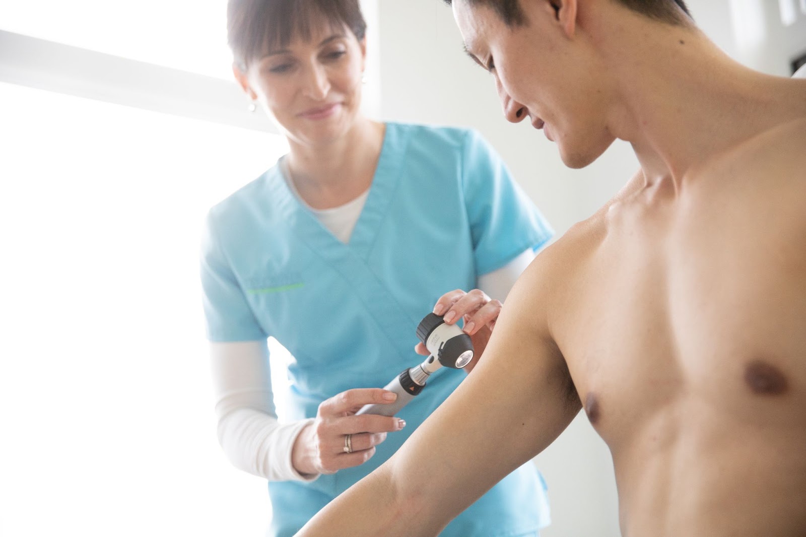 A clinician examines a patient's upper arm with a dermatoscope.