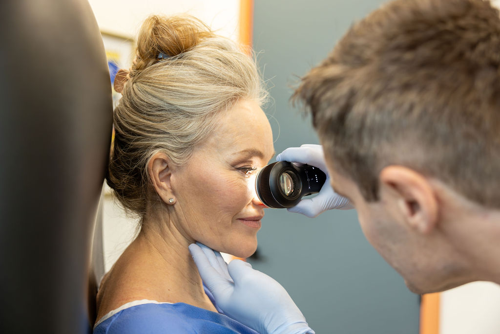 A clinician examines a patient's face with a dermatoscope.