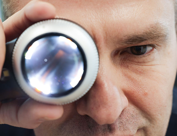 Close-up of a clinician holding a dermatoscope to one eye.