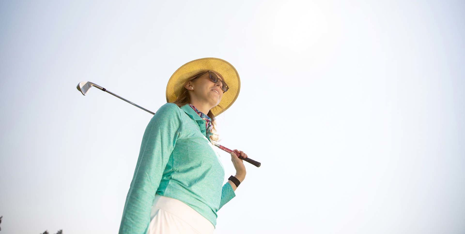 woman holding a golf club wearing an anti-aging sun hat and sun protective clothing
