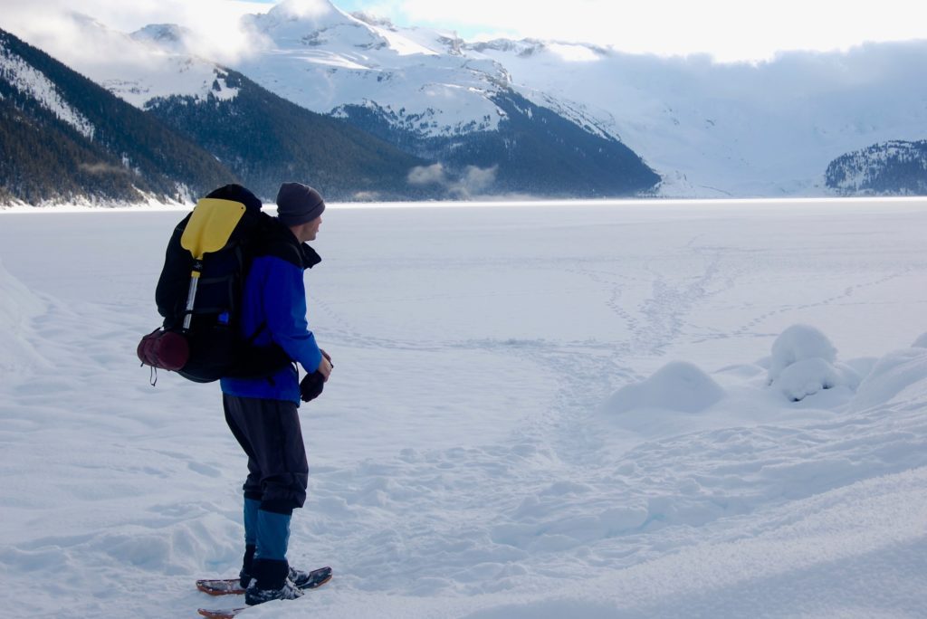 Man snowshoeing with mountains behind him relating to wearing sunscreen in the winter.