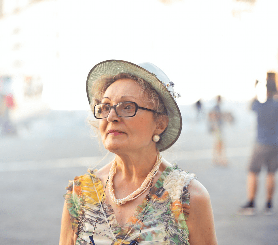 elderly woman standing outdoors wearing a hat and glasses, highlighting seniors uv sun protection