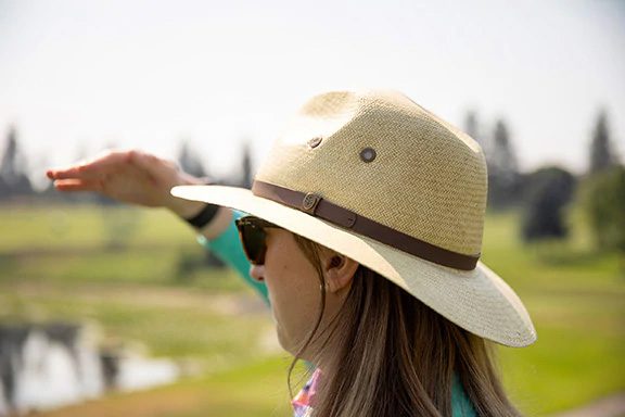 woman wearing anti-aging sunglasses and a sun protective hat while playing golf, shielding her eyes from the sun