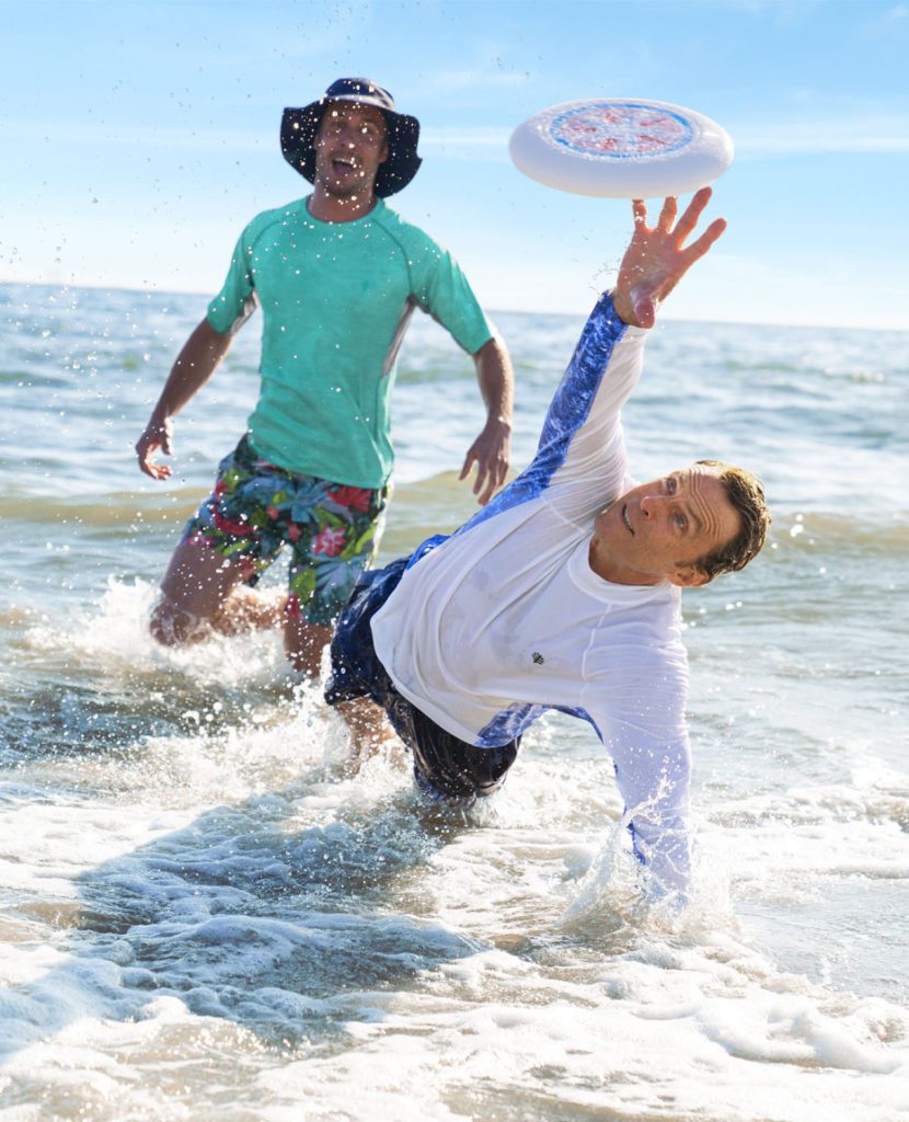 Two men playing frisbee in the water wearing sun protection, highlighting sun protection misconceptions